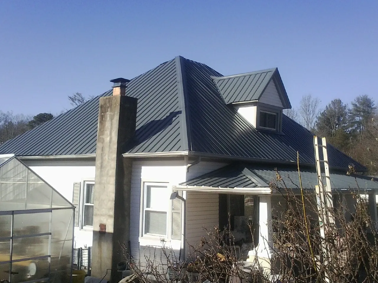 Dark blue standing seam metal roof on a white farmhouse with dormer — Slate & Tile Roof Repair by Roofing Brothers in Wells