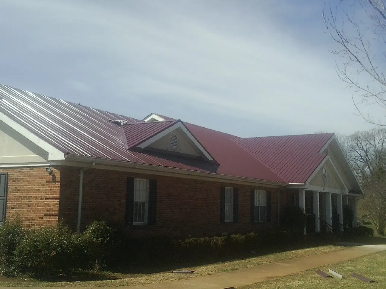 Red metal roof with gabled entries on a long brick building, from a Hail Damage Roof Repair job in Wells
