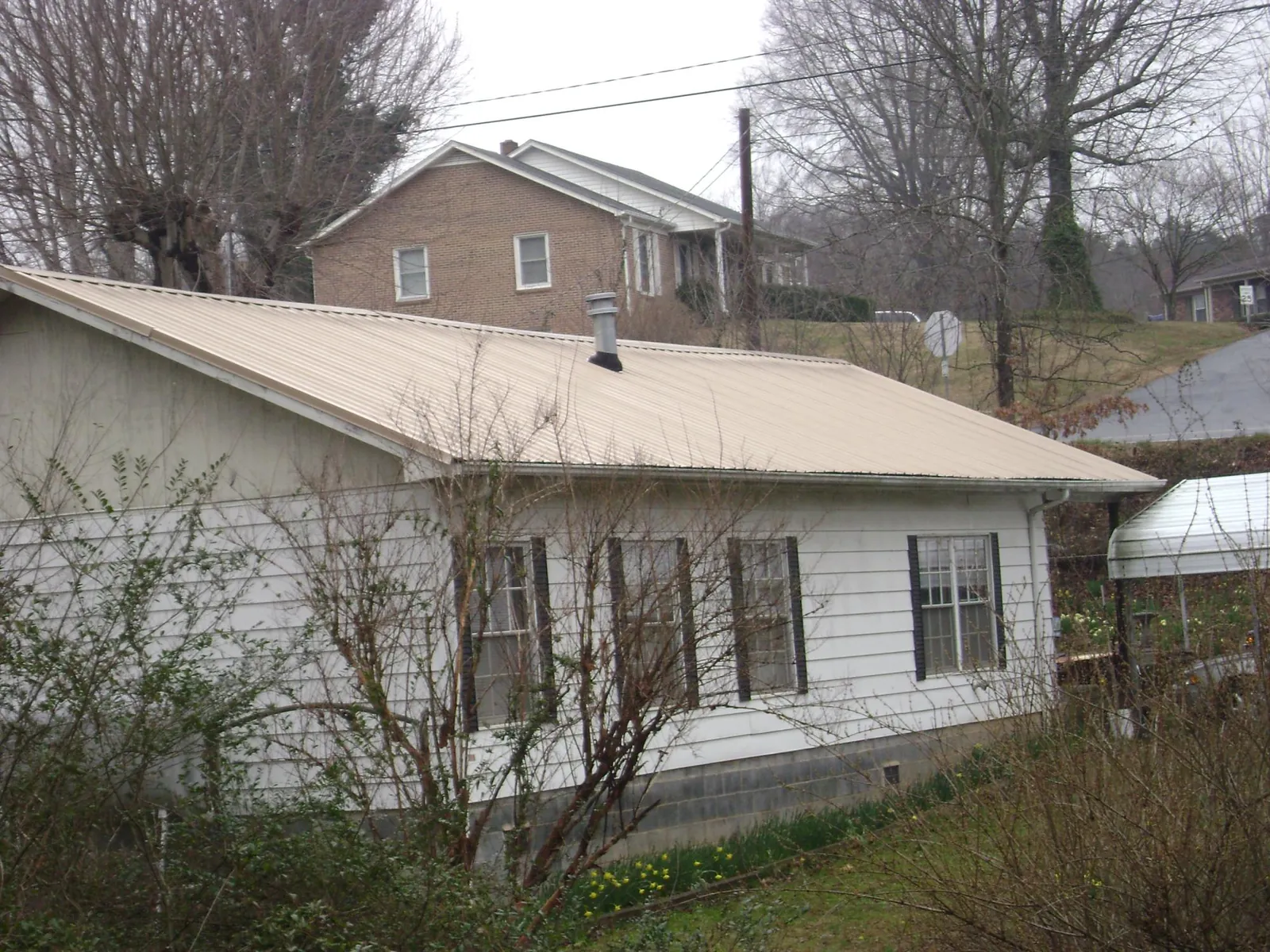Tan metal roof on a white sided house set into a hillside — Commercial Roofing by Roofing Brothers in Wells